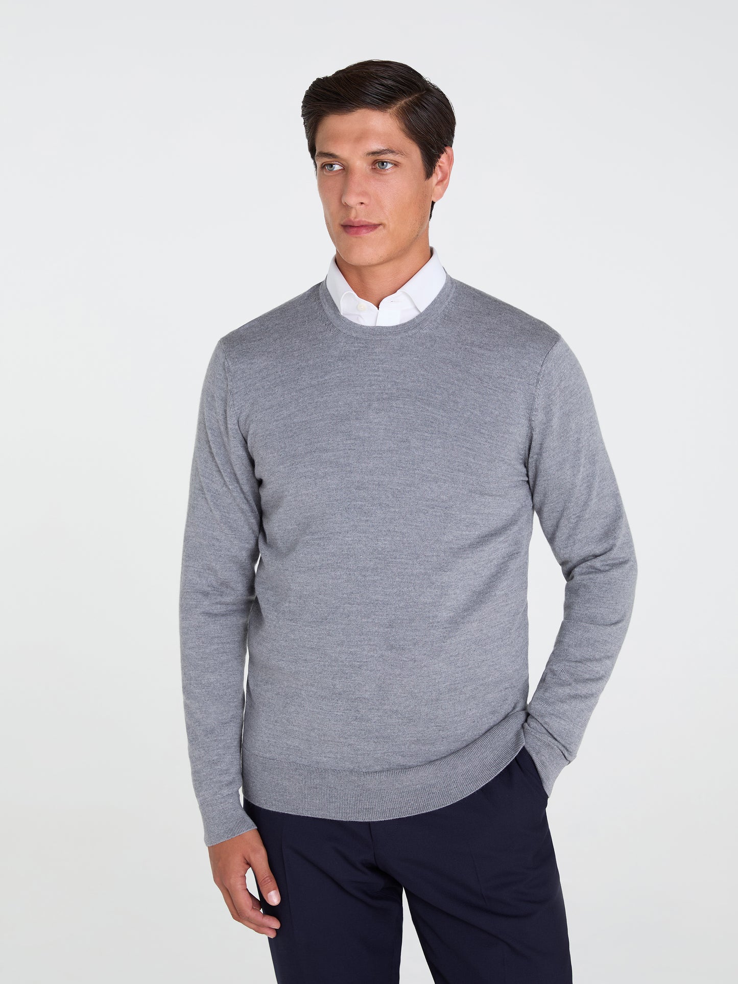 Man wearing a gray sweater over a white shirt with navy pants on a light gray background
